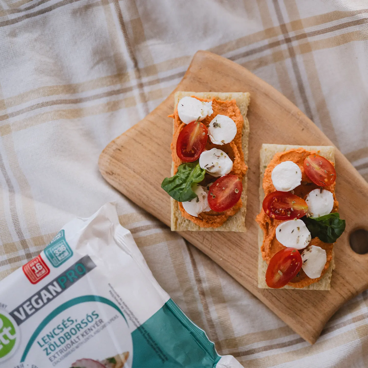 Two Abonett Vegan Pro crackerbread slices topped with a spread, cherry tomatoes and spinach, beside the Vegan Pro pack