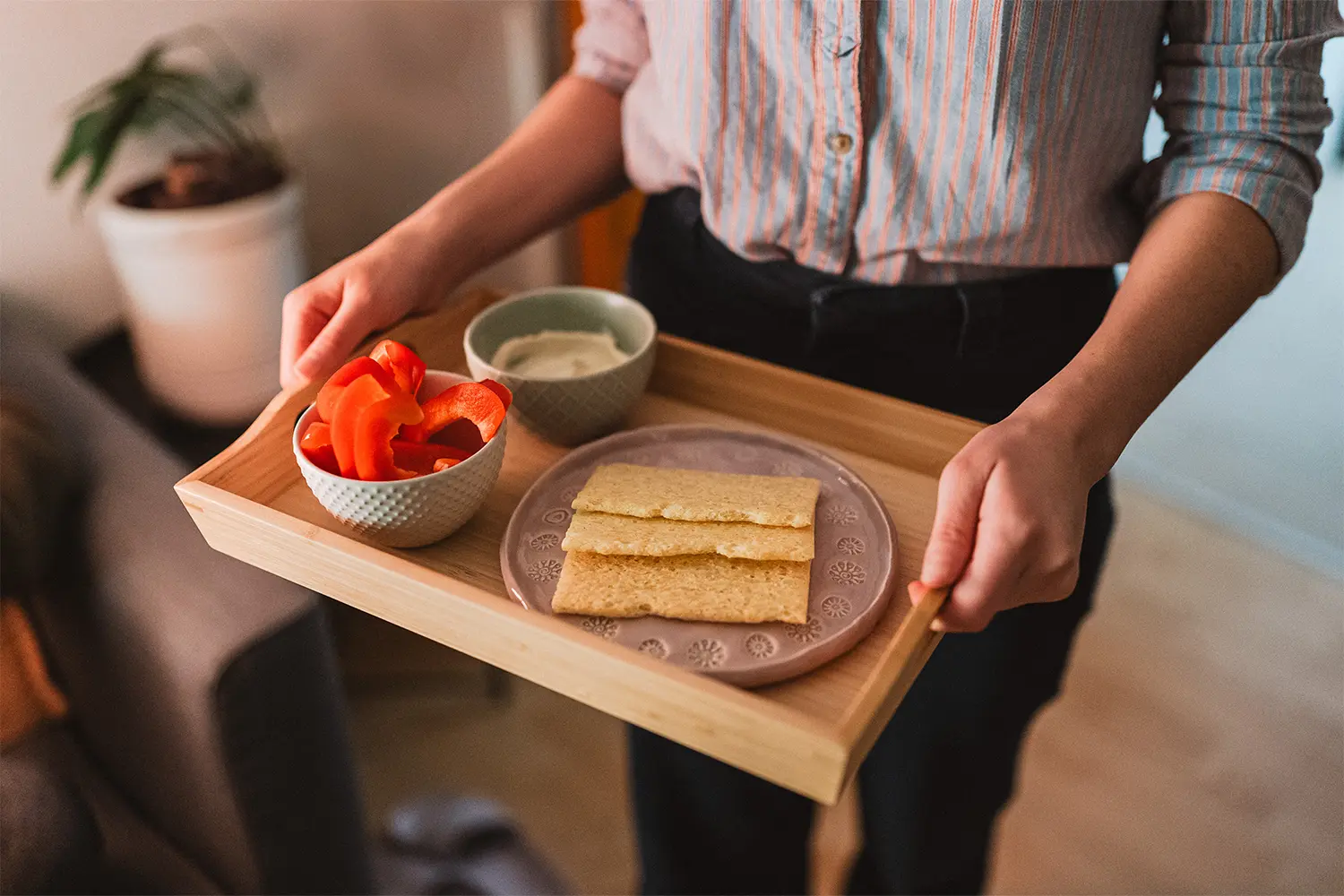 Crackerbread on a plate with sliced red pepper and a dip, carried on a wooden tray